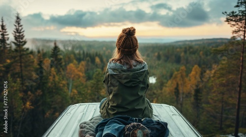 Person in a warm hat sitting on a rooftop overlooking a forest at sunset nomad van life pacific north west