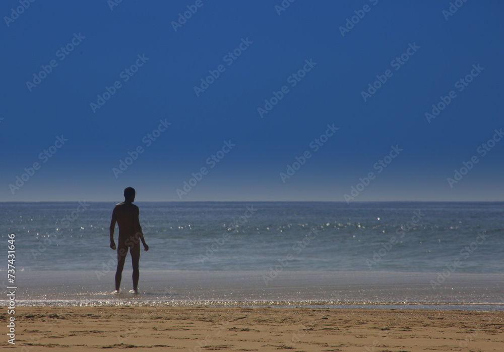 Man stands on the beach and looks at the ocean