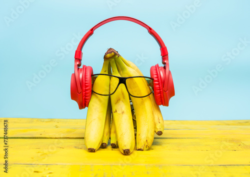 Creative ripe bananas in musical headphones and sunglasses. Bananas listening to music on a wooden yellow background. Ripe vitamin fruit banana