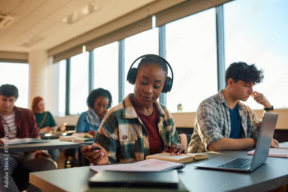 Black female student with headphones learning at college classroom.