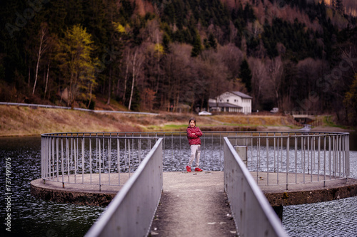 Child in a Red Jacket Standing on a Pier Leading to a Circular Platform on a Lake