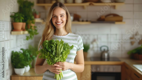 beautiful smiling young woman with a bunch of greens on the background of a white kitchen, proper nutrition, salad, celery, weight loss, lifestyle, health, girl, food, cooking