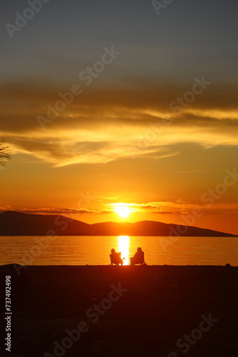 two people talking by the sea at sunset and a lonely fishing boat in the sea