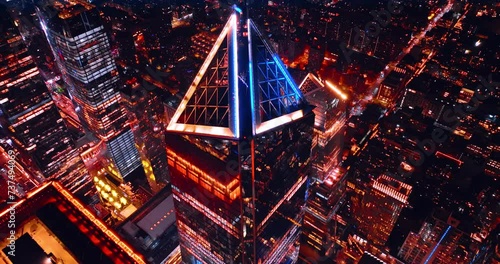 Rising above the sharp top of a skyscraper with neon light on. Top perspective on the luminous New York at night.