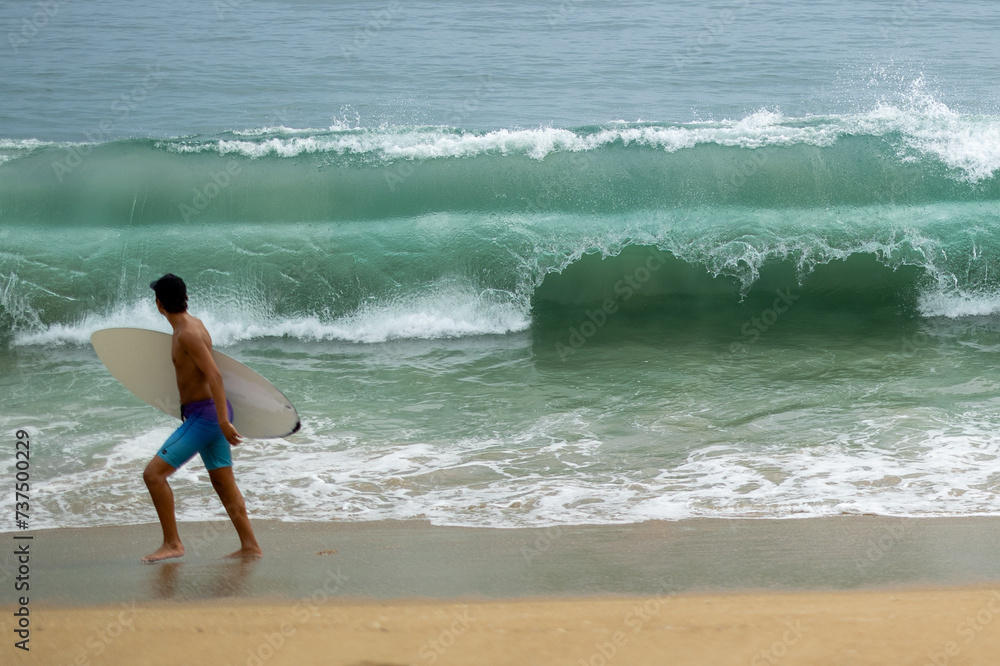 a man carries his surfboard into the ocean with big waves coming a man carries his surfboard into the ocean with big waves coming