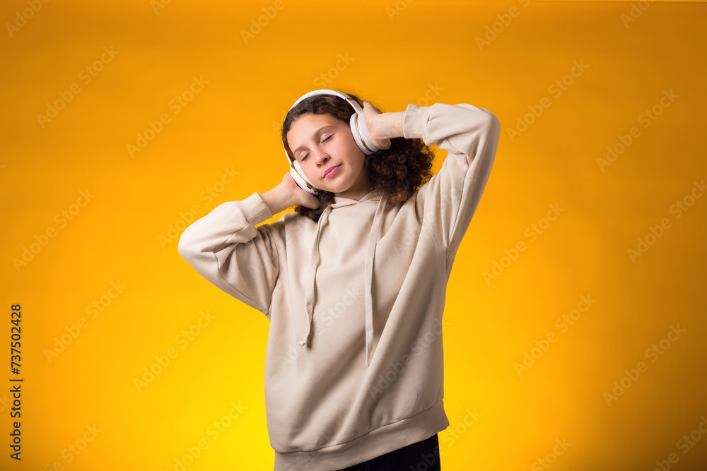 Smiling girl enjoying music in headphones on yellow background. Lifestyle and leasure concept Smiling girl enjoying music in headphones on yellow background. Lifestyle and leasure concept
