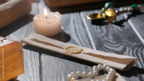 Shot of the table with paper and candle. Vintage rolled up envelope letter sealed with wax stamp laying on the table surrounded by candles and accessories.