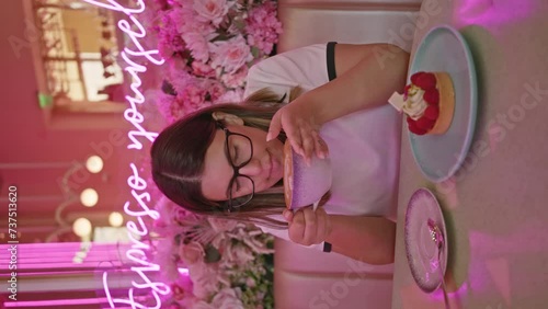 Young woman enjoying dessert in a pink-themed cafe with neon lights and floral decor.