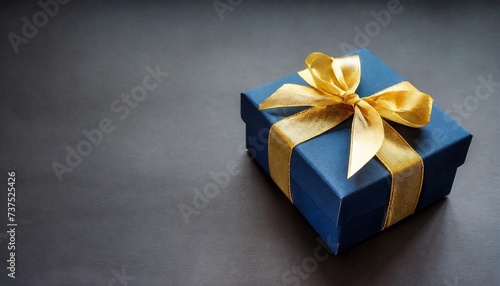 blue gift box with golden ribbon bow elegant dark blue present box with golden bow on a black background copy space background for greeting card for birthday christmas new year anniversary