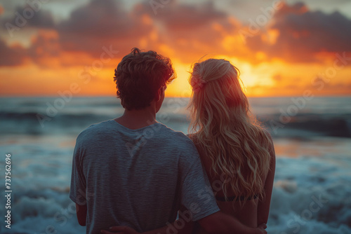 Man with arm around woman looking at sunset on beach