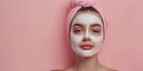 Beautiful young woman with a cosmetic mask on her face on a pink background

