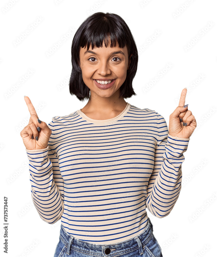 Young Hispanic woman with short black hair in studio indicates with both fore fingers up showing a blank space. Young Hispanic woman with short black hair in studio indicates with both fore fingers up showing a blank space.