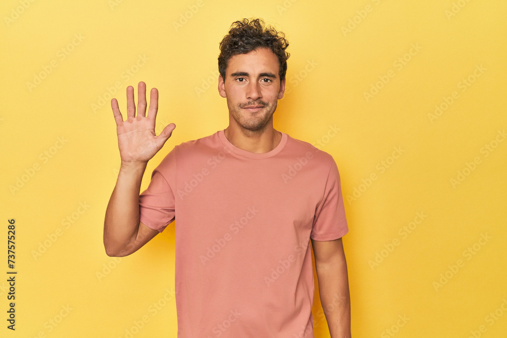 Young Latino man posing on yellow background smiling cheerful showing number five with fingers. Young Latino man posing on yellow background smiling cheerful showing number five with fingers.