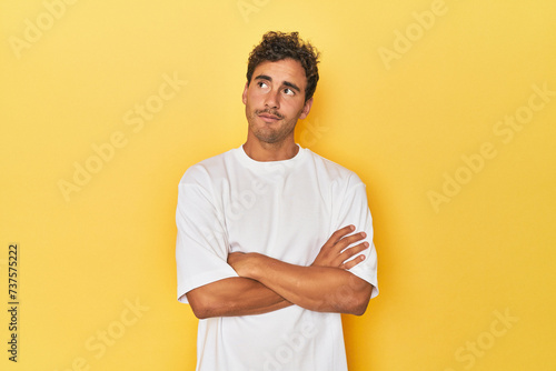 Young Latino man posing on yellow background dreaming of achieving goals and purposes