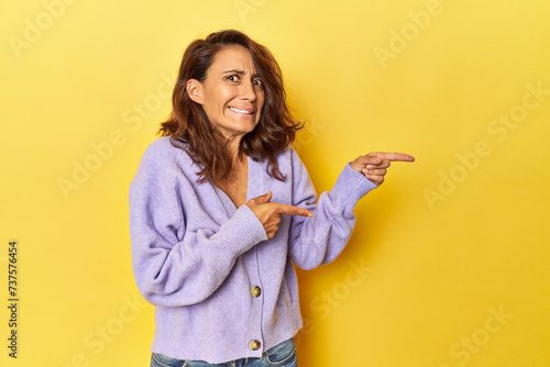 Middle-aged woman on a yellow backdrop shocked pointing with index fingers to a copy space. photo