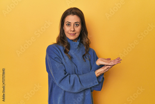 Middle-aged caucasian woman on yellow holding a copy space on a palm. © Asier