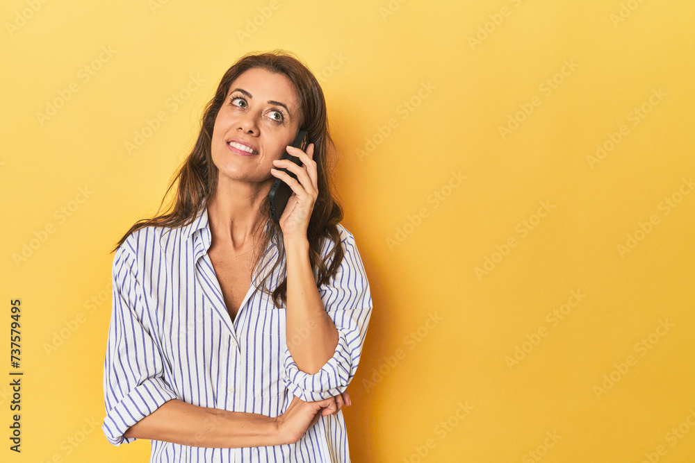 Middle aged woman using mobile phone in a yellow studio setting Middle aged woman using mobile phone in a yellow studio setting