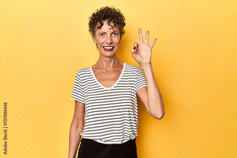Mid-aged caucasian woman on vibrant yellow cheerful and confident showing ok gesture. Mid-aged caucasian woman on vibrant yellow cheerful and confident showing ok gesture.