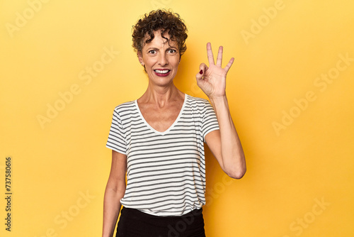 Mid-aged caucasian woman on vibrant yellow cheerful and confident showing ok gesture.