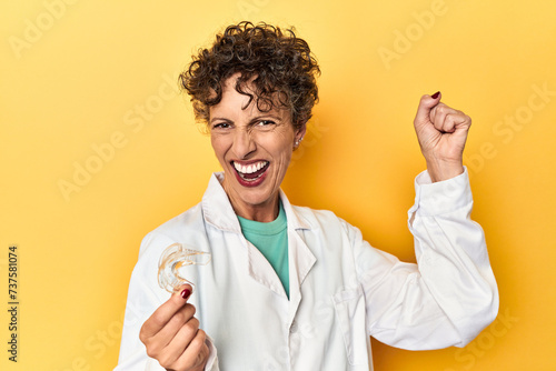 Doctor with invisible dental aligner on yellow raising fist after a victory, winner concept.