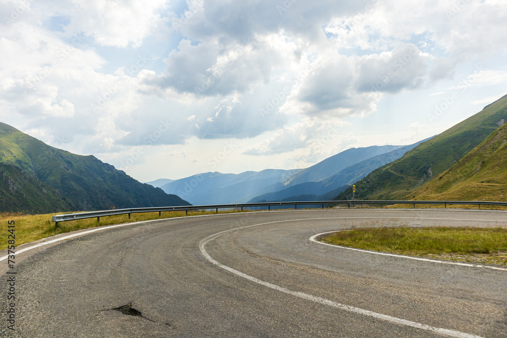 Mountain road in summer. Beautiful curved road, rocks, stones, blue sky with clouds. Landscape with empty highway through the mountain pass in summer. Travel