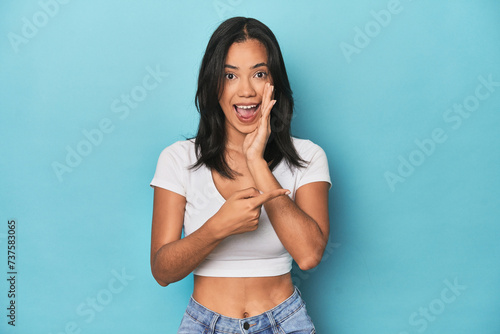 Filipina young woman on blue studio saying a gossip, pointing to side reporting something.
