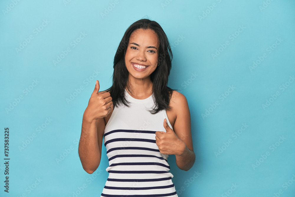 Fototapeta premium Filipina young woman on blue studio raising both thumbs up, smiling and confident.
