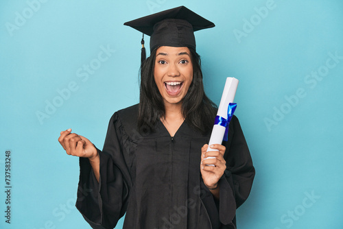 Celebrating Filipina graduate with diploma and cap on blue studio