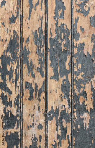 Vertical photo of an old wooden boards painted with dark paint, which has partially peeled off due to time and weather conditions