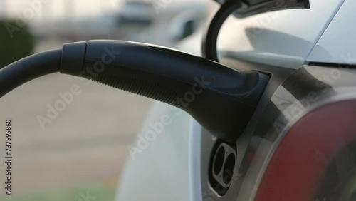 Close up shot of a female hand charging electric car, plugging in charger into the EV