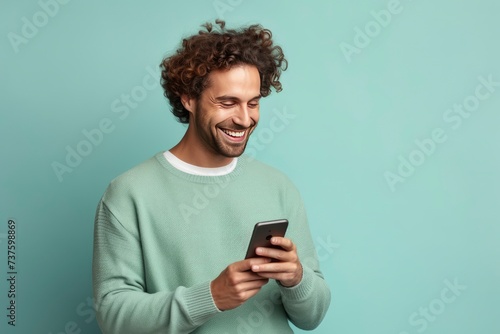 fun young man wear knitted sweater hold in hand use mobile cell phone look aside on workspace isolated on plain pastel light blue cyan background studio portrait - generative ai photo