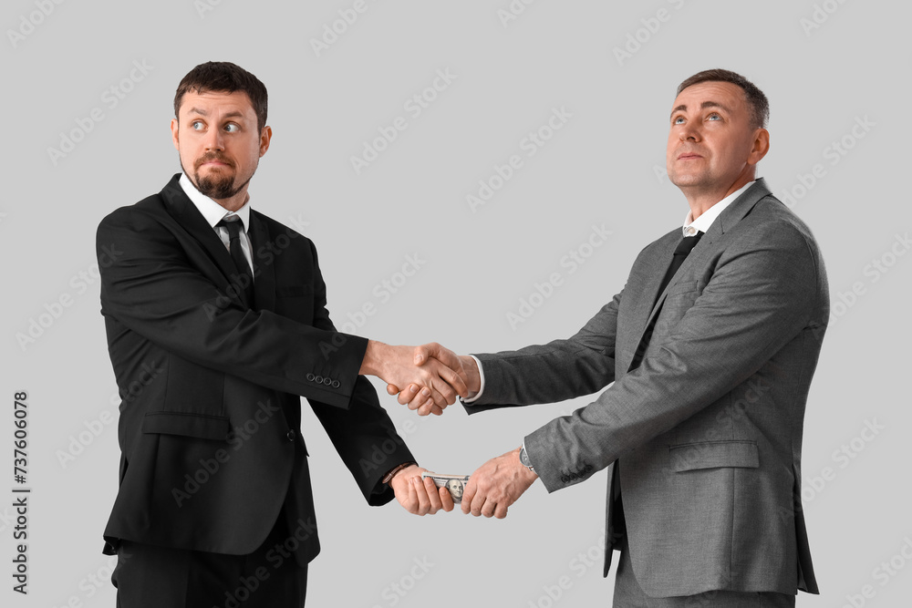 Business men with bribe shaking hands on grey background Business men with bribe shaking hands on grey background