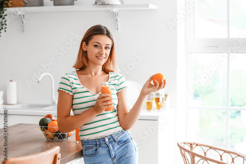 Young woman with bottle of juice and orange in kitchen