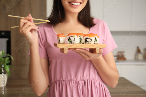 Young woman eating tasty sushi rolls in kitchen