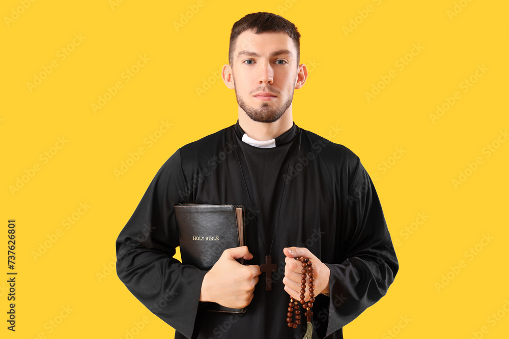 Young priest with Holy Bible and praying beads on yellow background Young priest with Holy Bible and praying beads on yellow background