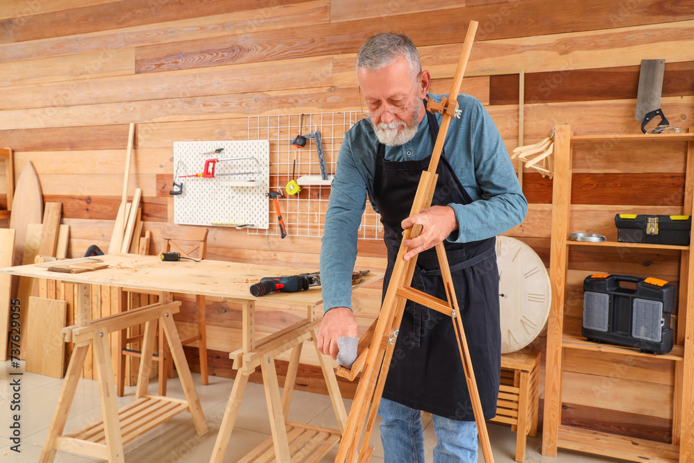 Mature carpenter working with wooden easel in shop