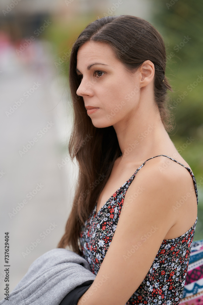 Young woman in a floral dress sitting outdoors, looking thoughtful with a blurred background. Young woman in a floral dress sitting outdoors, looking thoughtful with a blurred background.