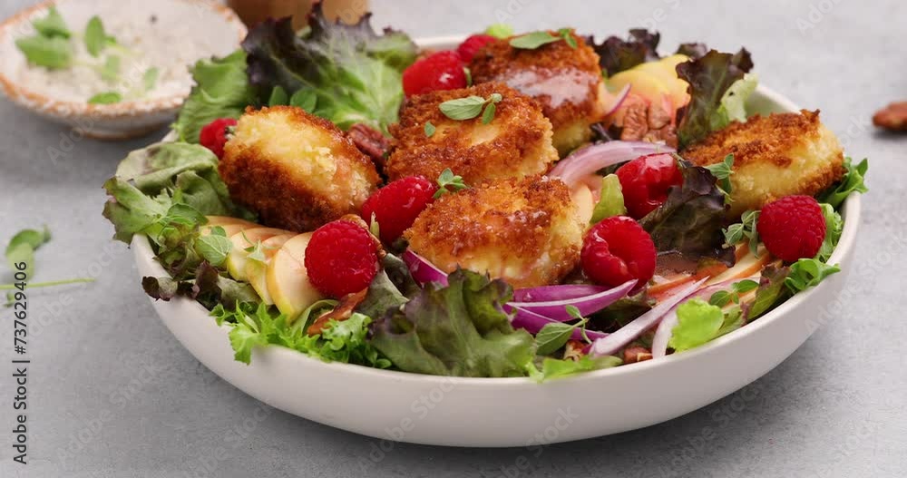 Fried goat cheese salad with raspberries and red onion and green salad, pouring dressing over Fried goat cheese salad with raspberries and red onion and green salad, pouring dressing over