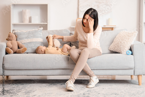 Young woman with toy and her baby suffering from postnatal depression on sofa at home