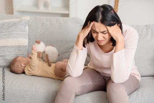 Angry young woman with her baby suffering from postnatal depression on sofa at home photo
