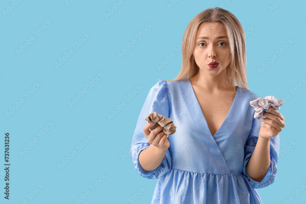 Thoughtful young blonde woman with scrunchies on blue background Thoughtful young blonde woman with scrunchies on blue background