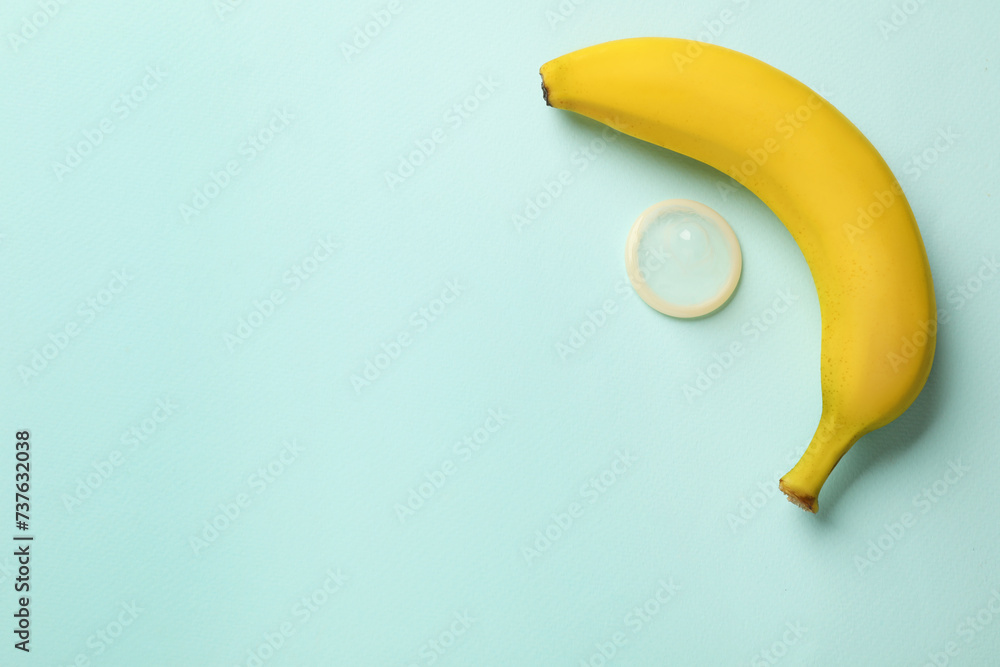 Banana and condom on turquoise background, flat lay with space for text. Safe sex concept