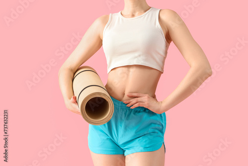 Young woman in sportswear with fitness mat on pink background