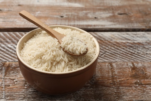 Raw basmati rice and spoon in bowl on wooden table, space for text
