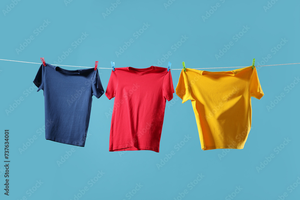 Colorful t-shirts drying on washing line against light blue background