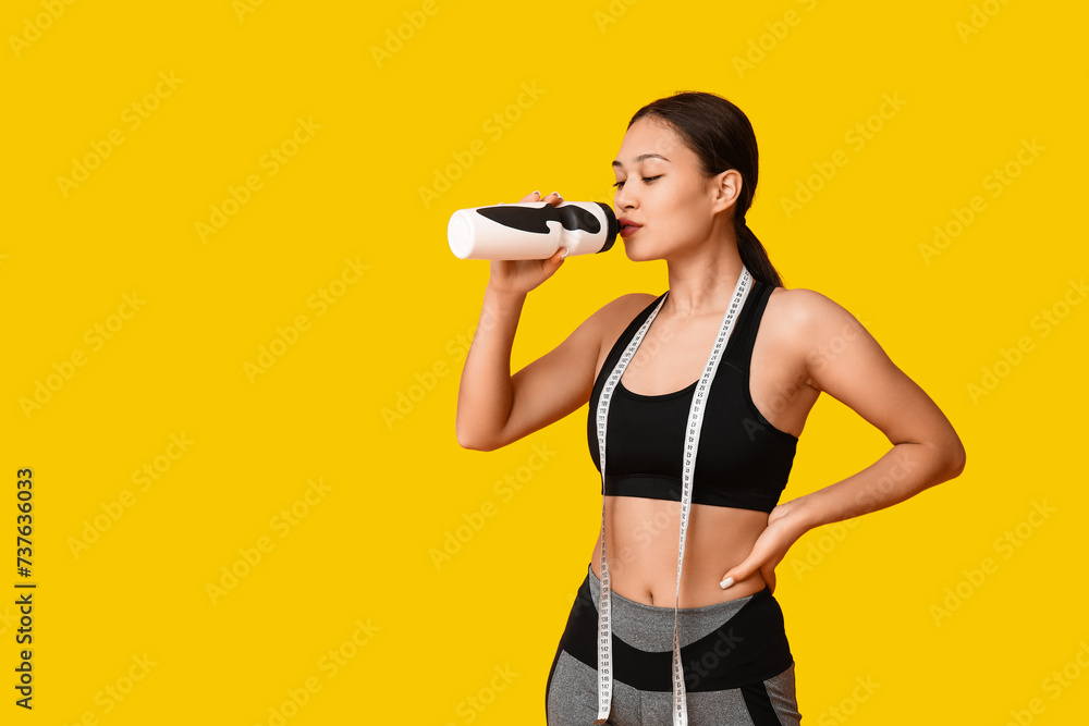 Young woman in sportswear and with measuring tape drinking water on yellow background. Weight loss concept Young woman in sportswear and with measuring tape drinking water on yellow background. Weight loss concept