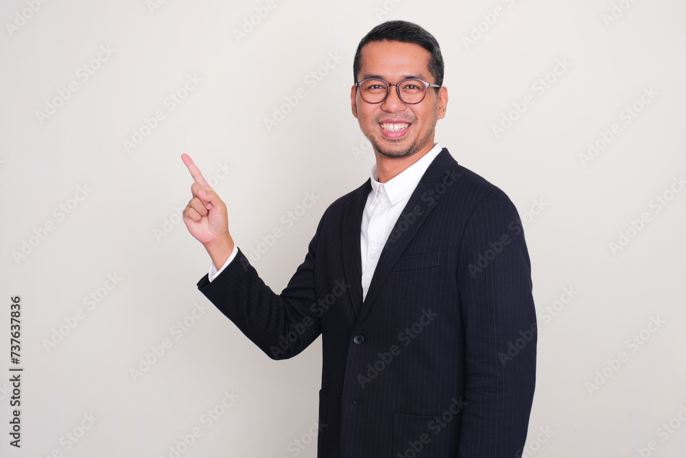 Asian businessman smiling at the camera with one hand pointing to upper right corner Asian businessman smiling at the camera with one hand pointing to upper right corner