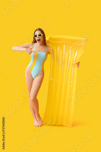 Surprised young woman in tank swimsuit and with inflatable mattress on yellow background © Pixel-Shot