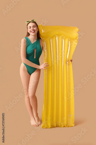 Pretty young woman in tank swimsuit and with inflatable mattress on beige background © Pixel-Shot