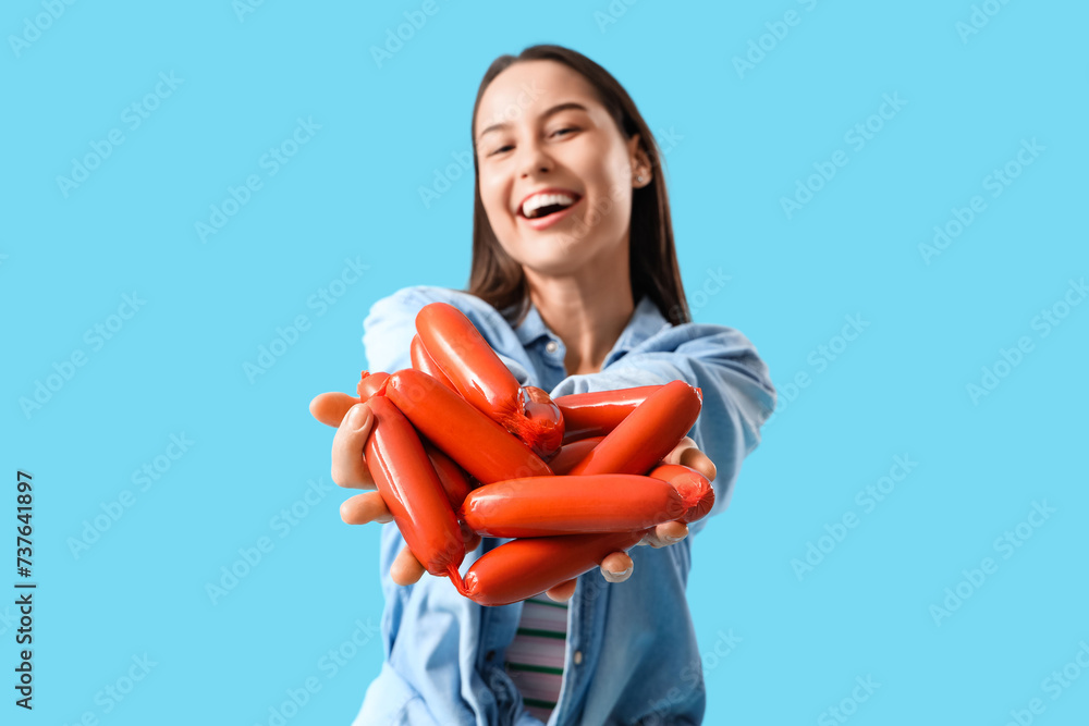 Young woman with tasty sausages on blue background Young woman with tasty sausages on blue background